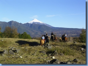 Group of riders on horseback in front of Villarrica Volcano on a horseback trail ride in chilean andes
